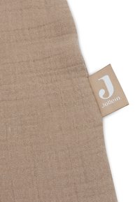 Tissu beige avec un motif tissé texturé, comportant une petite étiquette avec le logo 'J' et le nom de la marque 'Jollein.'