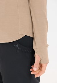 Beige langærmet top med tommelhuller, lavet af blødt stof. Sorte bukser med en logoed waistband. Tekstureret, tætsiddende design.