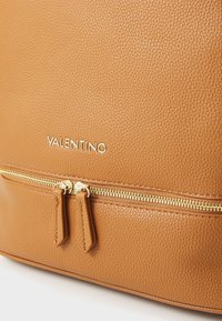 Borsa a mano in pelle marrone con finitura testurizzata, dotata di una zip dorata e del logo "VALENTINO" stampato sulla parte anteriore.