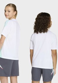 Deux enfants portant des chemises blanches à manches courtes et des shorts gris avec des accents pastel se tiennent côte à côte, l'un faisant face à l'avant et l'autre à l'arrière.