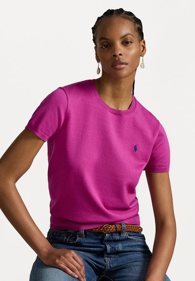 T-shirt rose à manches courtes dans une coupe classique, avec un col rond et un logo brodé. Associé à un jean en denim bleu et une ceinture tissée marron.
