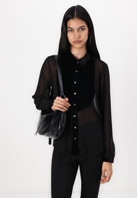 Camisa preta transparente de mangas longas com colarinho de veludo, frente com botões, combinada com calças pretas e uma bolsa de imitação de couro preta.
