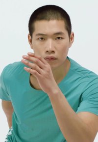 Atlet v krátkym rukávom, teal športovým tričkom s okrúhlym výstrihom, predvádza predný pohyb s vystretou rukou.