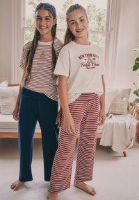 To piger iført hverdagstøj: den ene i en rød- og hvidstribet t-shirt med mørkeblå bukser, den anden i en hvid t-shirt med grafik og røde stribede bukser.