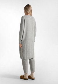 Grünes Strick-Loungewear-Set bestehend aus einem langen Pullover und einer engen Hose, mit entspannter Passform, strukturiertem Stoff und hellbraunen Clogs.