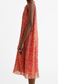 Robe sans manches à motifs rouges avec des plis, présentant une silhouette évasée ample, un tissu texturé et un détail à nouer au niveau du col.