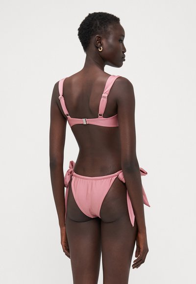 Rosa bikini med justerbare stropper, en spenne bak og en høy-kuttet bunn med knytedetalj på sidene. Glatt tekstur.