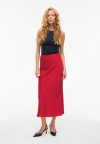 Röd midjekjol i satin med mjuk textur och lätt glans. Matchas med en svart figursydd topp och svarta klackskor.