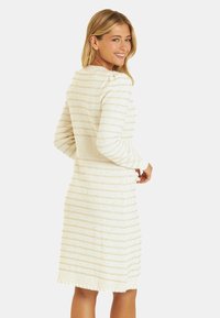 Abito maglione color crema con righe testurizzate e orlo frangiato. Presenta una vita aderente e maniche lunghe per una silhouette rilassata.