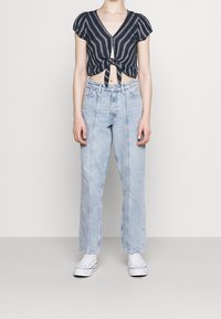 Marinblus med vita ränder, kort och puffärmad, med knyt framtill, kombinerad med ljusblå höga raka jeans och vita sneakers.