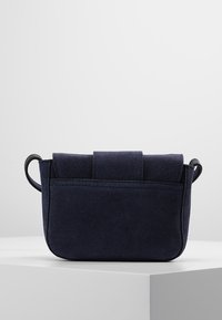 Tmavě modrá semišová kabelka se strukturálním tvarem, obsahující překrývající se vrch a boční ucha. Hladký povrch s jemným prošíváním.