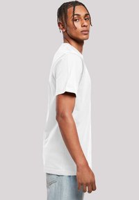 Hvit kortermet t-skjorte laget av myk bomull, med klassisk rund hals og avslappet passform. Sett fra siden, brukt sammen med lyseblå jeans.