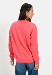 Koralle Sweatshirt mit lockerer Passform, gerippten Bündchen und Saum. Glattes Baumwollmaterial mit klassischem Rundhalsausschnitt und dezentem Detail auf der Rückseite.