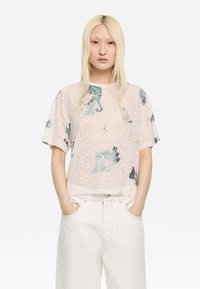 Korte mouwen, lichte blouse in lichtroze met abstracte zeelevenprints in blauw, groen en zwart. Losse pasvorm met een ronde halslijn.