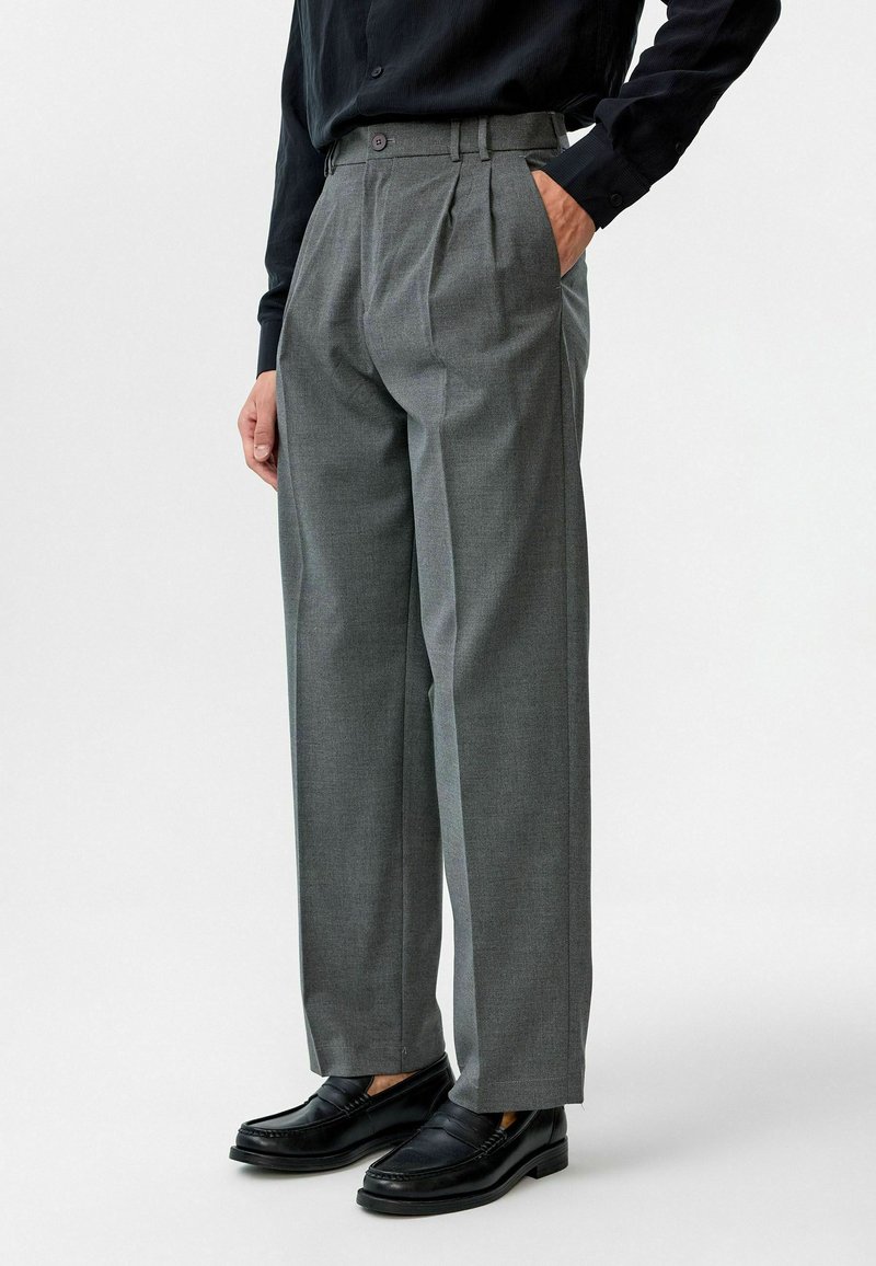 Grijze geplooide broek van geweven stof, met een hoge taille en zijzakken, gecombineerd met zwarte leren instappers.