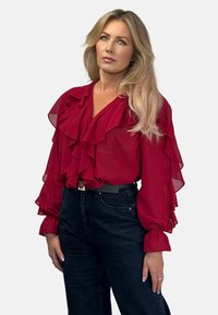 Czerwona bluzka z szifonu z falbanami z przodu i rękawami, w zestawie z ciemnymi dżinsami z wysokim stanem. Posiada czarny pasek z srebrną klamrą.