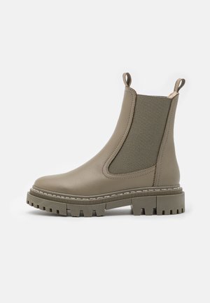 Olive green leather ankle boot with elastic side panels and pull tabs, featuring a thick, rugged rubber sole and white stitching details.