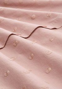 Tessuto rosa chiaro con una texture liscia, caratterizzato da delicate motivi ricamati di piccoli disegni floreali in rilievo, distribuiti uniformemente sulla superficie.
