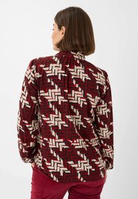 Long-sleeve shirt featuring a bold red, cream, and black geometric pattern, with a relaxed fit and smooth fabric texture.