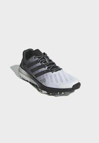 Zapatilla deportiva en negro y gris con parte superior de malla, que presenta tres franjas negras, suela texturizada y un prominente "210" en el costado.