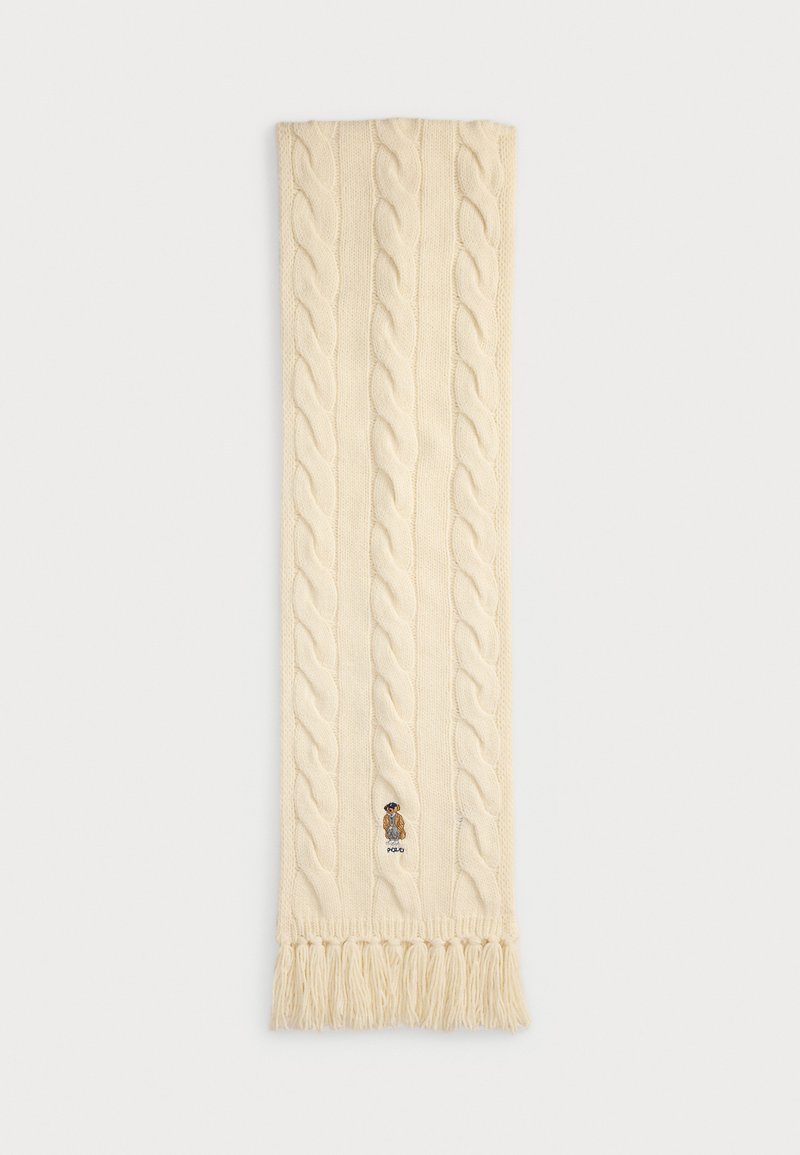 Bufanda crema de punto con patrón de trenzas, extremos con flecos y un logo bordado que presenta un personaje de oso. Material de lana suave y texturizada.