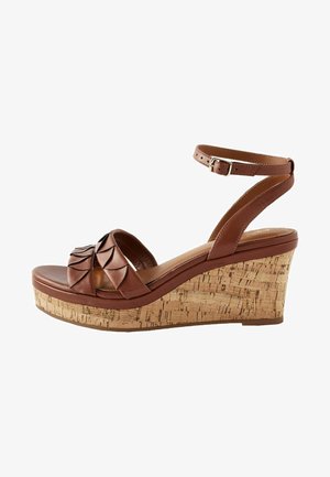 Sandales à talons compensés en cuir marron avec une semelle en liège, présentant un design de bride pliée et une fermeture à boucle à la cheville. Semelle intérieure en douceur.