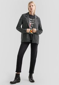 Szary teksturowany żakiet na czarnej koszulce z grafiką. Połączony z czarnymi spodniami slim-fit i botkami na kostkę z detalami w postaci pasków.