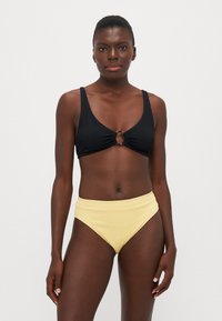 Svart texturerad bikiniöverdel med en cirkulär guldfinish; kombinerad med högmidjade, ribbade gula bikiniunderdelar.