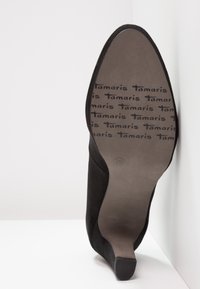 Černá semišová lodička na vysokém podpatku se špičatou špičkou. Podešev nese opakující se logo a velikost 39. Hladká a matná textura.