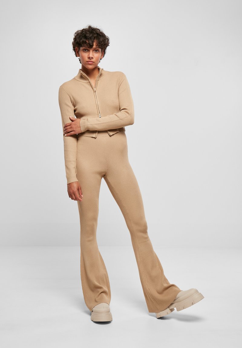 Beige ribbat stickad träningsdräkt med dragkedja vid kragen, åtsittande topp och utsvängda byxor. Klumpiga beige plattformssneakers fulländar looken.