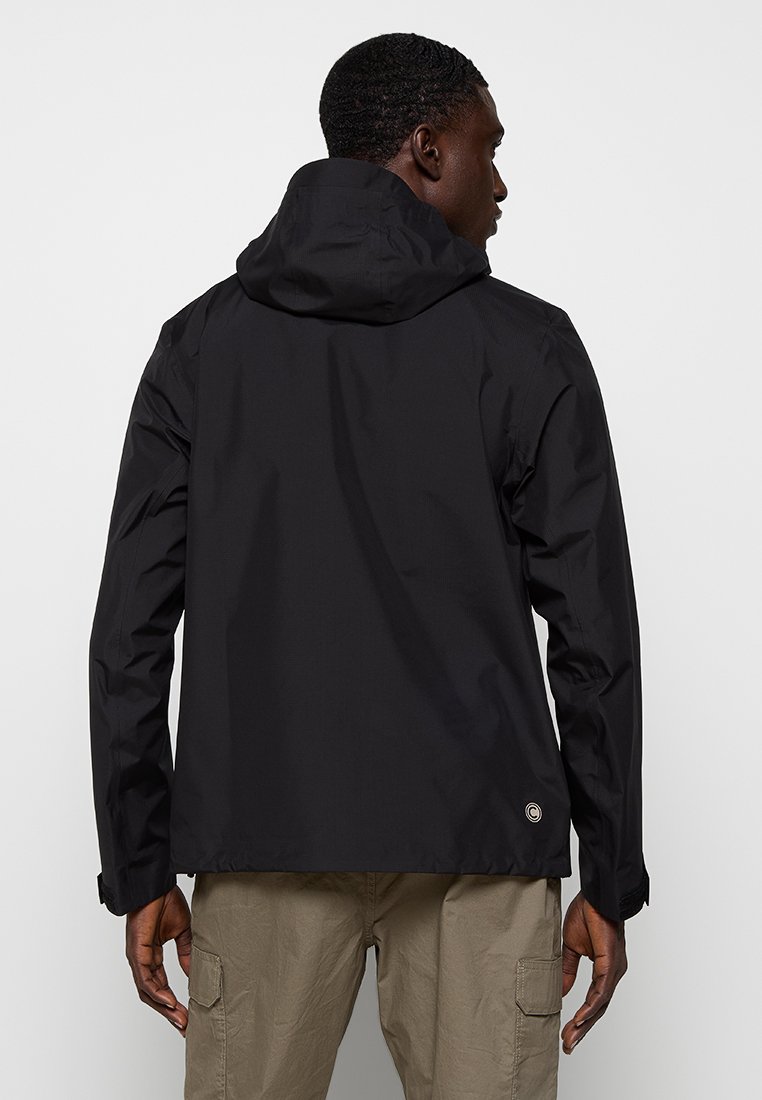 Giacca nera impermeabile con cappuccio, caratterizzata da una texture liscia e un logo rotondo sulla parte bassa della schiena. Design minimalista, senza chiusure visibili.