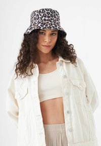 Chapeau seau à imprimé léopard avec un large bord, fabriqué en tissu lisse. Porté par un mannequin, associé à une veste en denim de couleur claire et à un top côtelé.