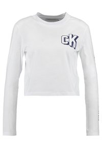 Weißes cropped Langarmshirt aus Baumwolle mit einem blauen "CK"-Logo auf der Brust und Textdesign entlang des Ärmels. Glatte Textur.