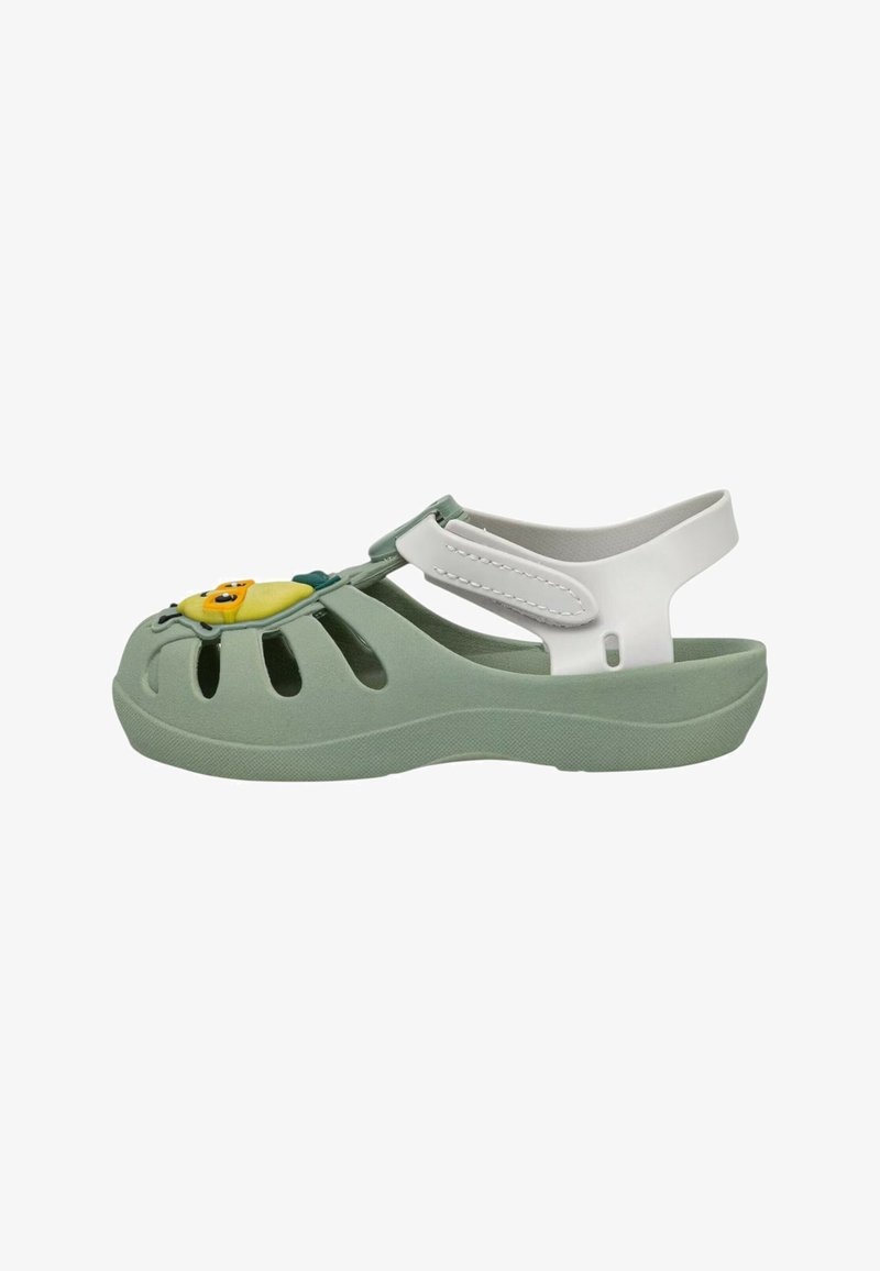 Infradito verdi in gomma con fori aperti, cinturino bianco per il tallone e un accento giocoso di un personaggio di cartone animato giallo sulla parte anteriore. Texture morbida, design leggero.