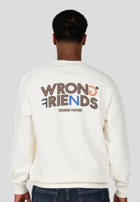 Sudadera blanca con "WRONG FRIENDS" en letras grandes y coloridas en la parte posterior. Cuello redondo, mangas largas, hecha de tela suave.
