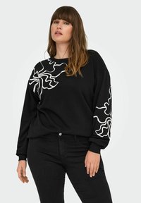 Black sweatshirt with long sleeves featuring white wavy floral design on one shoulder and arm. Cotton material, relaxed fit. Denim pants.