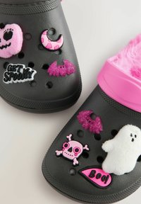 Melnas koka kurpes ar rozā akcentiem, kurām ir dažādi Halovīnu tematikas dekorācijas: skelets, ķirbis, spoks, sikspārnis un uzraksti "Get Spooky" un "Boo." Mīksta rozā oderējuma.