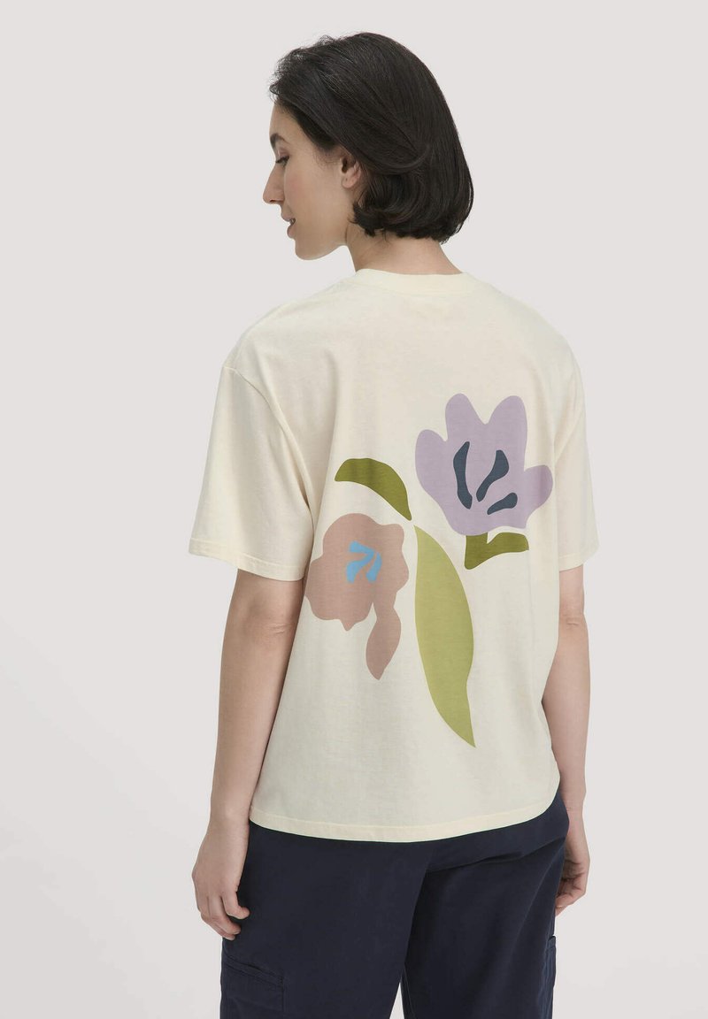 Romige katoenen T-shirt met een bloemenontwerp op de achterkant, voorzien van roze, paarse en groene accenten. Korte mouwen en een relaxte pasvorm.