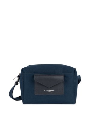 Trousse de toilette rectangulaire bleu marine avec poche avant en cuir noir et sangle pour le poignet, marquée "Lancaster Paris" sur la poche.