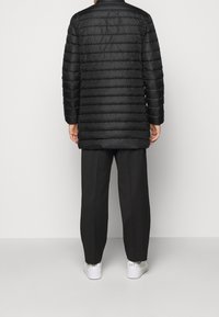 Svart puffjacka med horisontell quiltning, knälång, med hög krage och långa ärmar, bärs över skräddarsydda byxor och sneakers.