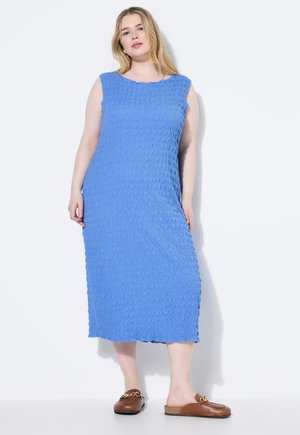 Abito midi senza maniche di colore blu con tessuto testurizzato caratterizzato da un motivo ondulato. Abbinato a scarpe slip-on marroni con dettaglio a catena.