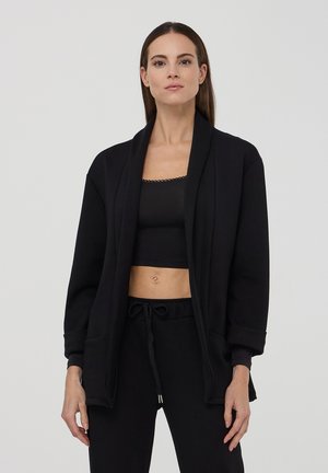Cardigan lungo nero con maniche a lunghe realizzato in tessuto morbido, con apertura frontale, tasche laterali e vestibilità comoda con colletto a scialle.