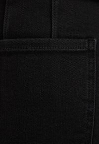 Zwarte denimstof met een gedetailleerde close-up van de zak, met zichtbare stiksels en een gladde, licht gestructureerde oppervlakte.