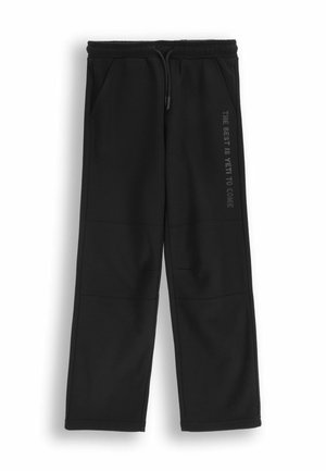 Czarne dresy z elastycznym paskiem w talii, sznurkiem i kieszeniami bocznymi. Charakteryzują się matowym nadrukiem na lewej nogawce. Miękka tekstura materiału.