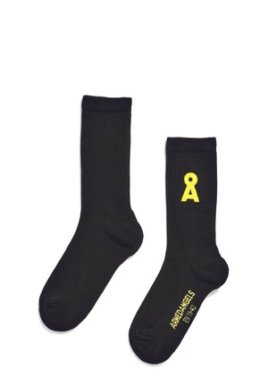 Chaussettes noir à côtes avec un logo jaune en forme de lettre "A" d'un côté et le texte de la marque sur le dessous. Tissu tricoté avec une texture lisse.