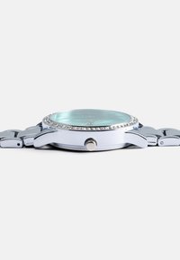 Montre-bracelet en métal argenté avec un cadran vert menthe, des accents ressemblant à des diamants autour de la lunette et une finition lisse et polie.