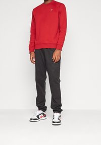 Röd sweatshirt, rund halsringning, ribbade mudd och nederkant. Matchad med svarta byxor och vita sneakers med röda accenter.