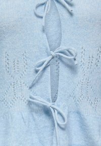 Šviesiai mėlynas megztinis su priekyje esančia nėriniuota raištelių uždarymo sistema ir subtiliais raštais prie apykaklės ir apačios.