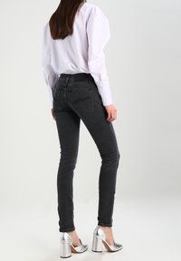 Tunna svarta jeans i denim med hög midja och blekta detaljer. Matchas med silvriga klackskor och en vit skjorta.