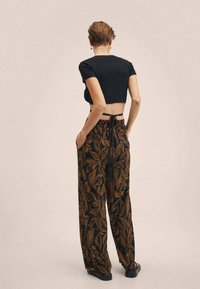 Zwarte cropped top met korte mouwen, gecombineerd met hoge taillebroeken met een bruin loofpatroon op een zwarte achtergrond.